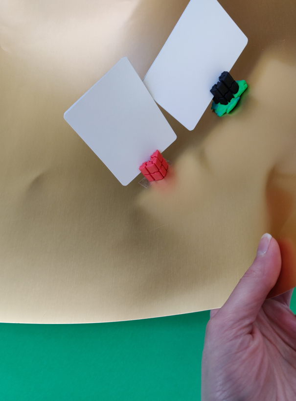 This shows two TI'TAINS holders adhered to a reusable shiny gold poster board.  The poster board is titled, showing that the holder stay in place due to the adhesives use (one uses double sided tape, and the other uses Play-Doh)