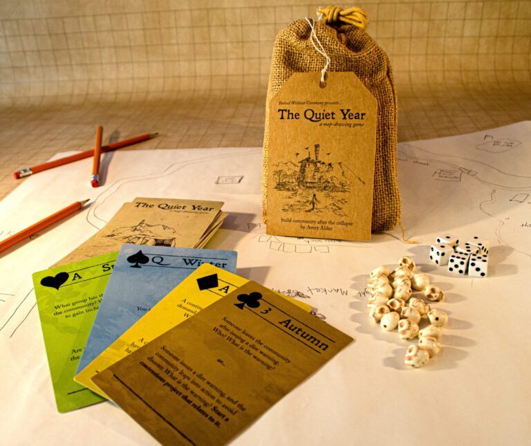 The contents of the bagged set for The Quiet Year, including a deck of cards, skull tokens, and dice.