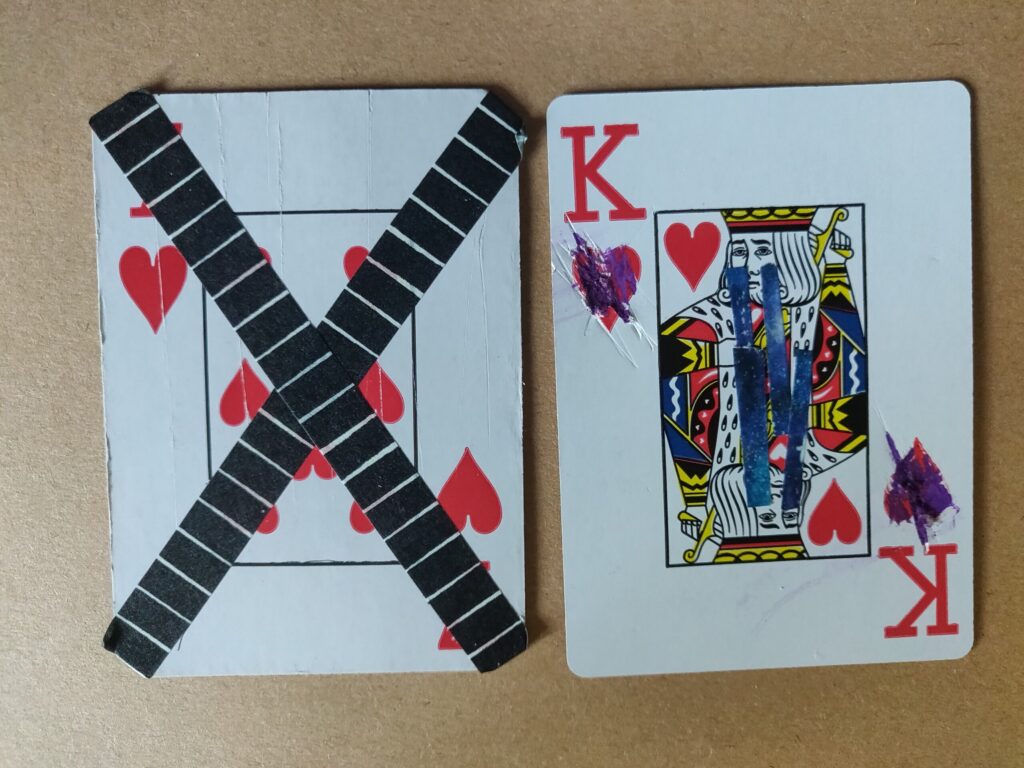 a photo of two modified cards
the first is a 7 of hearts that has been folded and dunked in water then crossed over with black lined tape
the second is a king of heards with the hearts scratch out and tape under the kings' eyes to make it look like he's crying (it was meant to be sad). 