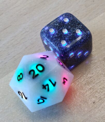 a photo of a d20 showing a 20 and lit up in rainbow and a d6 showing a 5 and lit up in blue