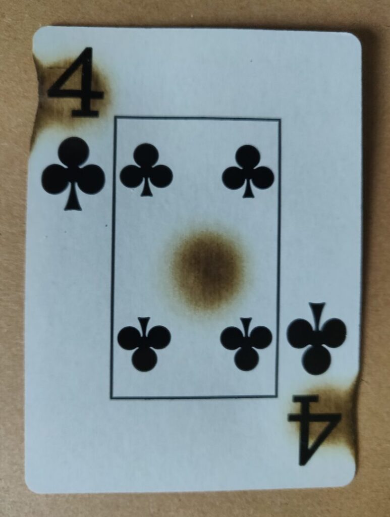 a photo of a 4 of clubs that's been burned at both locations where the number is shown and in the center of the card