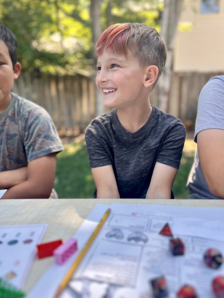 a photo of a kid sitting at a table covered in character sheets and dice, looking excitdely to the left