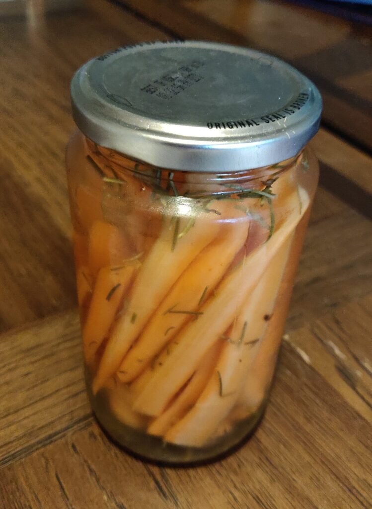 a glass jar full of cut up carrot sticks and soaking in a vinegar and rosemary pickling solution