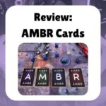 Review: AMBR Cards shows a photo of the AMBR cards, all flipped over and laid out across a gaming table with minis and dice and a map