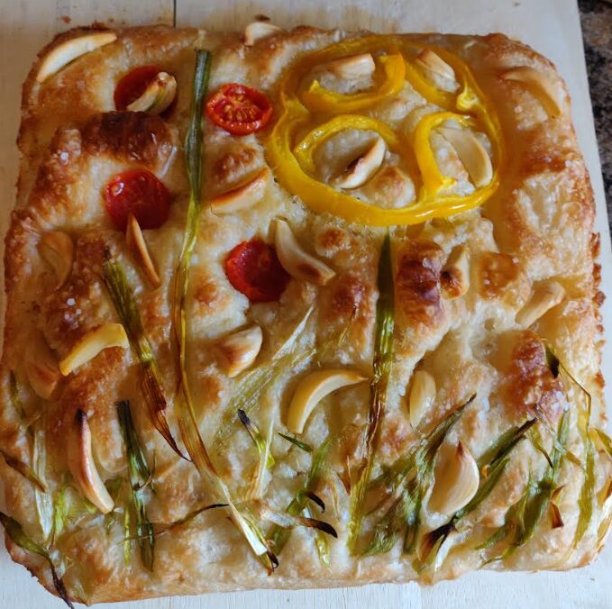 A photo of a focaccia decorated with vegetables (peppers, green onion, tomatoes, garlic)